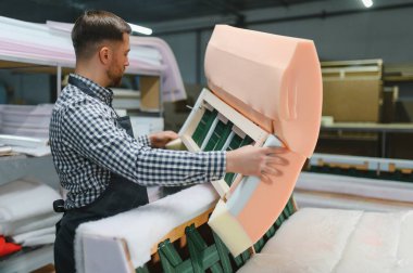 Marangoz şık bir kanepeyi, hareketli bir mobilya fabrikasında köpük ve ahşap kullanarak ustalıkla monte ediyor.