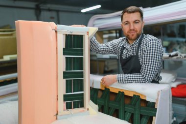 Marangoz, hareketli bir mobilya fabrikasında bir kanepe çerçevesi inşa etmek için özenle çalışıyor. Yetenekli bir işçilik ve detaylara dikkat çekiyor.