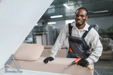 Marangoz modern bir kanepeyi hareketli bir mobilya fabrikasında ustalıkla monte ediyor, el işi ve kaliteye olan bağlılığını sergiliyor.