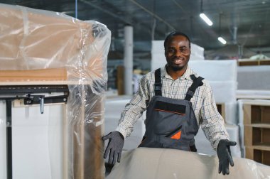 Bir mobilya fabrikasında kanepe üretimi yapan Afro-Amerikan işçisi, ahşap ve malzemelerle çevrili bir CNC makinesi kullanıyor.