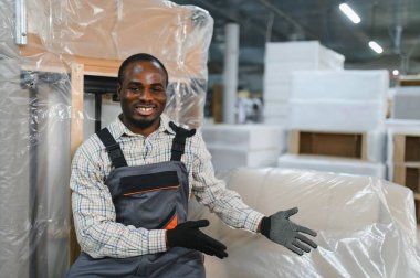 Gülümseyen Afro-Amerikan işçiler güzel sarılı bir kanepeyi mobilya fabrikası deposunda sunuyorlar.