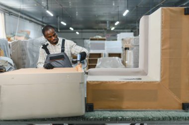 Marangoz, bir mobilya fabrikasında şık bir kanepe kuruyor. İşlerin yoğun olduğu bir ortamda pnömatik çivi tabancası kullanıyor.