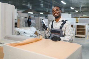 Marangoz bir mobilya fabrikasında kanepeyi ustalıkla döşeyip, üretimdeki hassasiyeti ve kaliteyi sağlamak için pnömatik çivi tabancası kullanıyor.