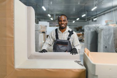 Gülümseyen marangoz, mobilya fabrikasındaki bir koltukta özenle çalışıyor. Her ayrıntıda beceri ve zanaatkarlık sergiliyor.