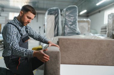 Adanmış işçiler, malzeme ve aletlerle çevrili bir mobilya fabrikasında dikkatlice bir kanepe monte ederek, işçilik ve üretim verimliliğini sergiliyorlar.