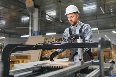 Marangoz güvenlik kaskı ve eldiven takıyor. Mobilya fabrikasında cnc makinesi kullanıyor. Kanepe üretimi için odun hazırlıyor.