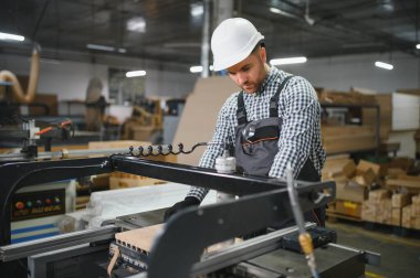 Güvenlik kaskı takan yetenekli bir marangoz, modern bir marangoz fabrikasında mobilya parçaları üretiyor.