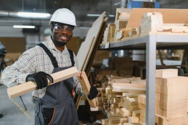 Ahşap bileşenleri inceleyen marangoz, hareketli bir fabrika ortamında mobilya üretiminde kalite ve hassasiyet sağlıyor.