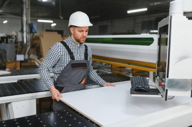 Marangoz güvenlik kaskı takıyor. Mobilya fabrikasındaki modern Cnc makinesine ahşap tahta yerleştiriyor.