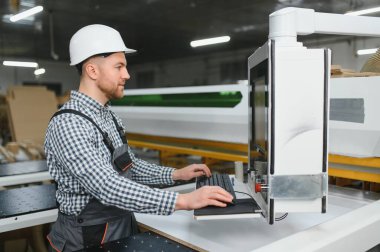 Bir mobilya fabrikasında güvenlik kaskı takan marangoz, üretim sürecini hassasiyetle kontrol ediyor.