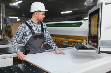 Mobilya fabrikasında çalışan bir işçi, bir CNC makinesi çalıştırıyor, kanepe üretimindeki hassasiyet ve verimliliğe odaklanıyor, koruyucu giysiler giyiyor.