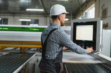 Marangoz güvenlik kaskı ve koruyucu ekipman takıyor, hareketli bir mobilya fabrikasında cnc makineleri çalıştırıyor, hassas ahşap ürünler üretiyor.