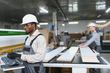 İki marangoz, bir mobilya fabrikasında mobilya üretimi için tahta kesen bir makineyle çalışıyor.