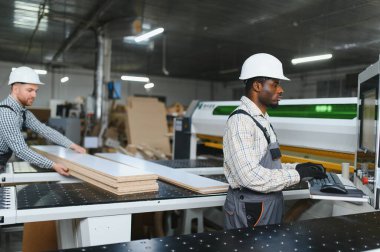 Modern cnc marangozluk makineleri kullanarak mobilya üreten iki fabrika işçisi, bir imalat ortamında takım çalışması ve hassasiyet sergiliyorlar.