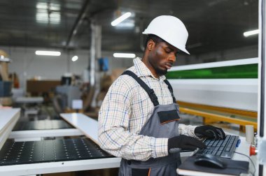 Modern bir mobilya fabrikasında güvenlik kaskı takan yetenekli bir marangoz gelişmiş üretim süreçlerini ön plana çıkarıyor.