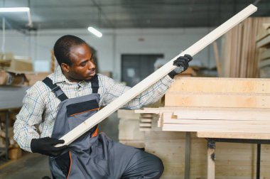 Becerikli marangoz mobilya fabrikasında ahşap bir kalası dikkatlice inceliyor, üretim sürecinde kalite ve hassasiyet sağlıyor.