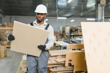 Marangoz koruyucu iş kıyafeti giyiyor mobilya fabrikasında büyük ahşap bir tahta taşıyor, kanepe ve ahşap işçiliği üretiyor.