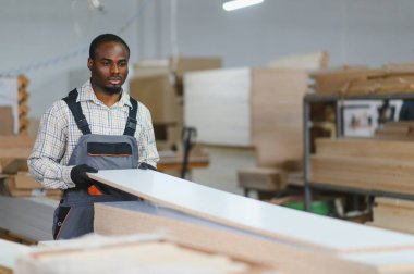 Marangoz eldiven ve tulum giyiyor. Yoğun mobilya fabrikasında ahşap döşemeleri dikkatlice yerleştiriyor.