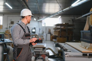 Bir mobilya fabrikasında güvenlik kaskı takan marangoz uzaktan kumandayla süreci kontrol ediyor.