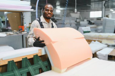 Marangoz, mobilya fabrikasında köpük kauçukla bir kanepeyi ustalıkla birleştiriyor, mobilya üretiminde zanaatkarlık sergiliyor.