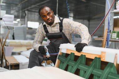 Marangoz bir mobilya fabrikasında kanepeyi ustalıkla monte ediyor, imalat sürecinde zanaat ve hassasiyet sergiliyor.