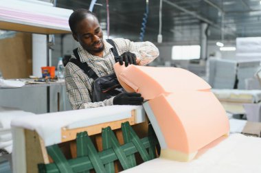 Afrika kökenli Amerikalı bir zanaatkar köpük kauçuk ve ahşapla ustalıkla çalışıyor, hareketli bir fabrika atölyesinde yüksek kaliteli mobilyalar yaratıyor.