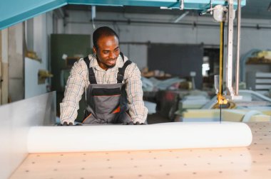 Afro-Amerikan işçiler bir mobilya fabrikasında ustalıkla bir cnc makinası çalıştırıyorlar, kanepe üretimi için hassas ahşap kesimine odaklanıyorlar.