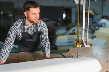 Marangoz elektrikli testere kullanıyor. Mobilya üretimi için köpüğü titizlikle kesiyor. Mobilya fabrikasında.