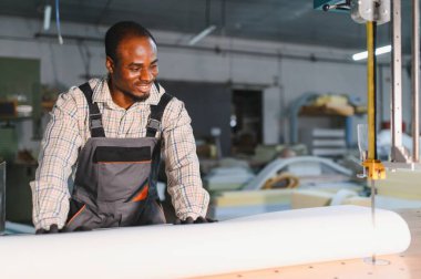 Gülümseyen marangoz, hareketli bir mobilya fabrikasında kumaş kesmek için testereyle testere kullanıyor.