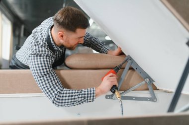 Marangoz, yoğun bir mobilya fabrikasında pnömatik tornavidayla kanepe mekanizması kuruyor. Yetenekli bir işçilik ve hassasiyet sergiliyor.