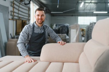 Zanaatkar gülümsüyor ve mobilya fabrikasında üretilen yeni kanepenin kalitesini kontrol ediyor.