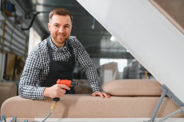 Marangoz, bir mobilya fabrikasında pnömatik tornavidayla kanepe monte ediyor. Yetenekli işçilik ve hassasiyet sergiliyor.