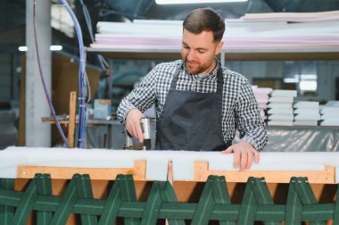 Marangoz pnömatik çivi tabancası kullanıyor, ahşap kanepe çerçevesini köpükle ve mobilya fabrikasında kayışlarla monte ediyor.