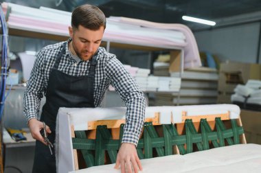 Marangoz kumaş kesiyor ve ahşap kanepeyi ustalıkla birleştiriyor. Mobilya atölyesinde çalışıyor.