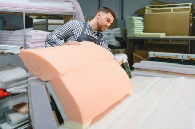 Marangoz, kaliteli işçiliğe adanmış bir mobilya fabrikasında ustalıkla çalışırken kanepe çerçevesine köpük yerleştiriyor.