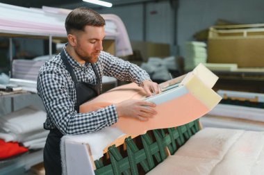 Marangoz mobilya fabrikasında kanepe monte ediyor, köpük ve ahşap ile çalışıyor, işine konsantre oluyor.