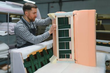 Marangoz, ahşap çerçeveler ve köpük yastıklar birleştiriyor. Mobilya fabrikasında kanepe yapımı için. Yetenekli işçilik sergiliyor.