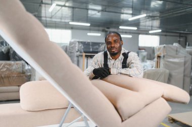 Mobilyacı kanepeye yaslanmış, fabrika deposunda üretim sürecini dikkatle inceliyor.