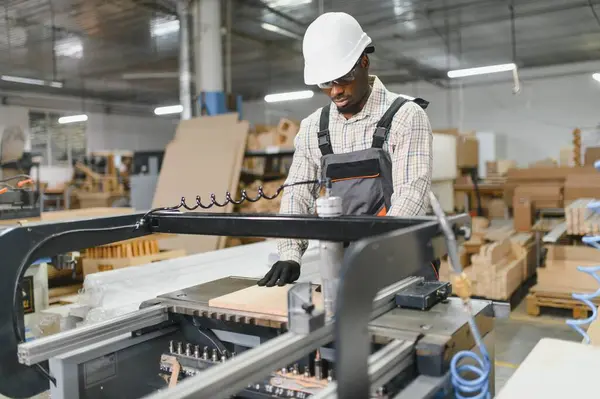 Yetenekli bir marangoz, yoğun bir mobilya fabrikasında kesin kesim ve şekillendirme için bir tahta parçasını dikkatlice yerleştiriyor.