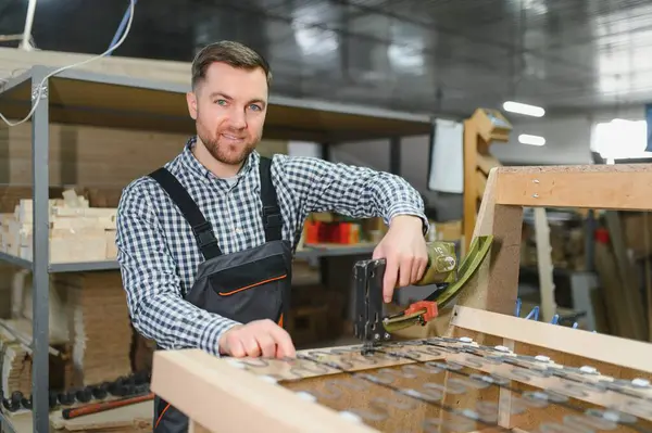 Marangoz bir mobilya fabrikasında çalışıyor. Kanepenin ahşap çerçevesini monte etmek için pnömatik zımba kullanıyor.