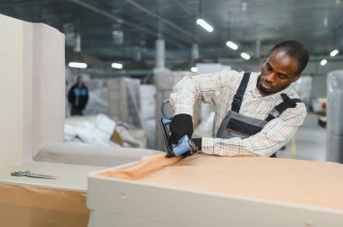 Mobilya üreticisi, yoğun bir mobilya fabrikasının hilesiyle çevrili, pnömatik zımba tabancasıyla bir kanepeyi destekliyor.