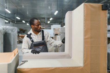 Marangoz, mobilya parçalarını hareketli bir kanepe fabrikasında ustalıkla birleştiriyor ve kaliteli ev mobilyalarının işçiliğine katkıda bulunuyor.