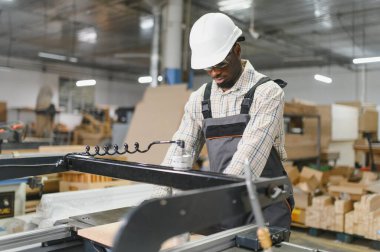 Marangoz güvenlik gözlüğü takıyor ve mobilya fabrikasında ahşap parçalar üreten ahşap bir makine çalıştırıyor.