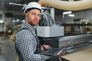 Marangoz dizüstü bilgisayarda cnc makineleri programlıyor, mobilya fabrikasında ahşap işlemeyi optimize ediyor, modern üretim tekniklerini sergiliyor.