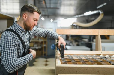 Marangoz bir mobilya fabrikasında özenle çalışıyor, çivi tabancasıyla kaliteli bir işçilik için sağlam bir tahta kanepe çerçevesi yapıyor.