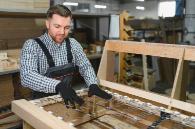 Marangoz, mobilya atölyesinde ahşap kanepe çerçevesine döşenmiş yayları dikkatlice kontrol ederek kalite ve konfor sağlıyor.