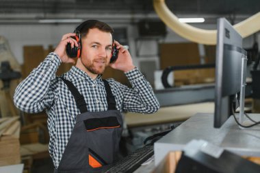 Marangoz, bir mobilya fabrikasında çalışırken işyeri güvenliğini sağlarken işitme koruması takıyor.