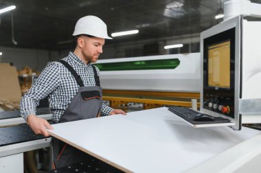 Marangoz mobilya fabrikasındaki modern cnc makinesine ahşap tahta yerleştiriyor, yüksek kaliteli mobilyalar için otomatikleştirilmiş üretim süreci başlatıyor