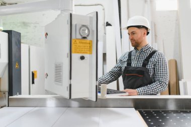 Bir mobilya fabrikasında güvenlik kaskı takan marangoz, üretimde hassasiyet ve verimliliğe odaklanıyor.