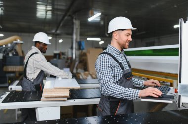 İki fabrika işçisi, ahşap mobilya parçaları üretimi sırasında bir cnc makinesi kullanıyor.